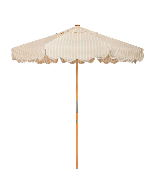 A beige and white striped patio umbrella with a scalloped edge and a wooden pole.