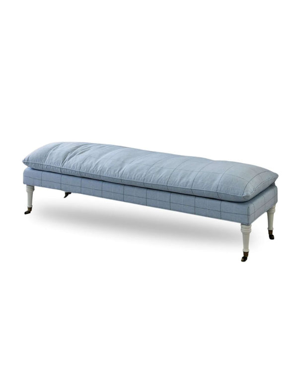 An upholstered bench with blue fabric, turned leg details, and metal casters.
