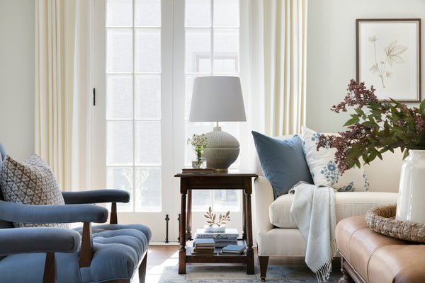 Living room with Off-white ceramic table lamp with brass accents. Blue and blue floral pillows on a white sofa.