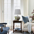 Living room with Off-white ceramic table lamp with brass accents. Blue and blue floral pillows on a white sofa.