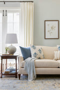 Living room with Off-white ceramic table lamp with brass accents. Blue and blue floral pillows on a white sofa.