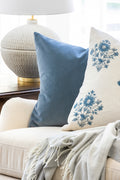 Living room with Off-white ceramic table lamp with brass accents. Blue and blue floral pillows on a white sofa.