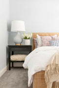 Bed frame designed with a natural mango frame and woven cane inset in bedroom with an off white comforter and pink throw pillows.